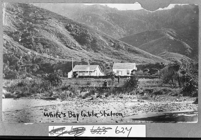 Historic White’s Bay cable station beside the beach below steep hills.